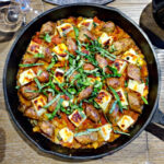 Cast iron skillet with baked Halloumi cheese, Italian sausage, and fresh basil in tomato sauce on table by The Hungry Songbird